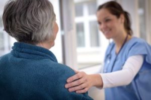 Female caregiver grasps senior female patient's shoulder