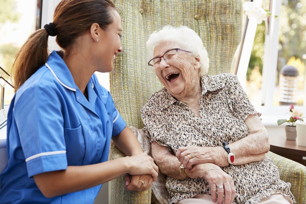 Senior woman sitting in chair and laughing with nurse